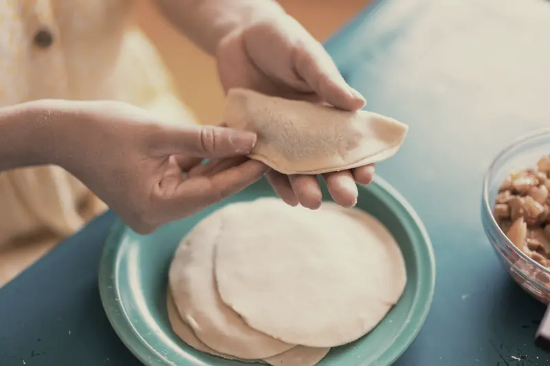 Handen die een schijf deeg dichtvouwen tot een pastei.